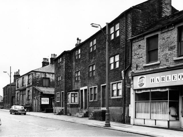 Town Street in August 1963. On the side of the garage wall next to 115 a sign promotes British Railways seaside excursions to Blackpool every weekday from 7th September. The train would leave Stanningley at 8.45am and would cost 15 shillings, today that would by 75 pence. In the centre the image houses numbers 119 to 125 with the Harlequin Cafe offering Coca-Cola, Pepsi-Cola and snacks at number 127 on the far right.