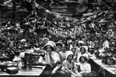 Staff seated at their Singer sewing machines at the firm of John Barran & Sons Limited, wholesale clothing manufacturers on Chorley Lane. The workplace was festooned with decorative bunting and paper chains, from which are suspended rosettes displaying the portrait of George V. The elaborate decorations are in celebration of his coronation which took place on June 22, 1911.