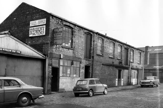 Industrial buildings on Aysgarth Road in October 1966. On the left is the licensed petroleum spirit store belonging to Regent Motors and Filling Station advertised above. The building in the centre is K. Shann & Sons Rag and Metal Merchants. An old fashioned oil lamp is hanging from the wooden lintel of the shop front. The building on the far right is a stables and three cars are parked on the street, the middle car is a Mini Cooper Reg: 372 HUA.