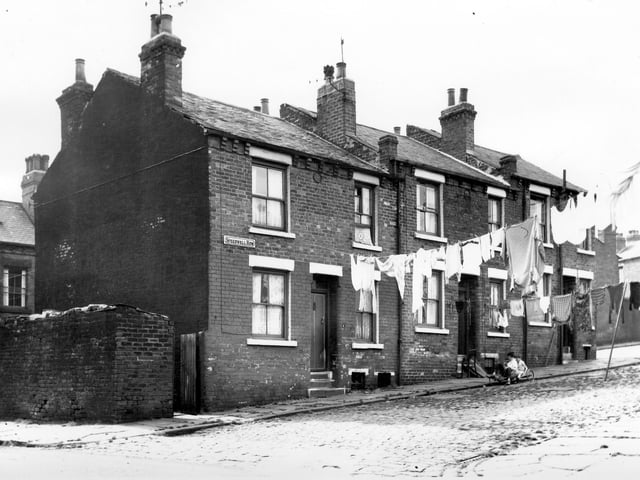 Two children sit on a homemade 'bogie' or go-cart. Seen from Cross Speedwell Street, view looks onto, three back-to-back properties on Speedwell Row, numbers run from 1 to 5 left to right. Washing hangs across the street