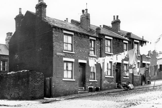 Two children sit on a homemade 'bogie' or go-cart. Seen from Cross Speedwell Street, view looks onto, three back-to-back properties on Speedwell Row, numbers run from 1 to 5 left to right. Washing hangs across the street