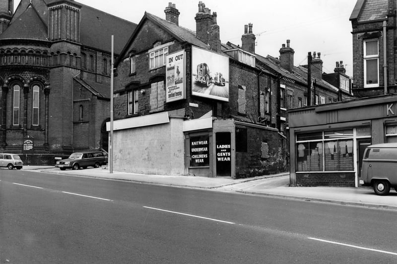 Wholesale clothing warehouse Roundhay Road pictured in April 1980. The front is boarded up and there are advertising hoardings on the upper floor. St. Aidan's Church is on the left with Elford Place leading off. On the right is Back Elford Place.