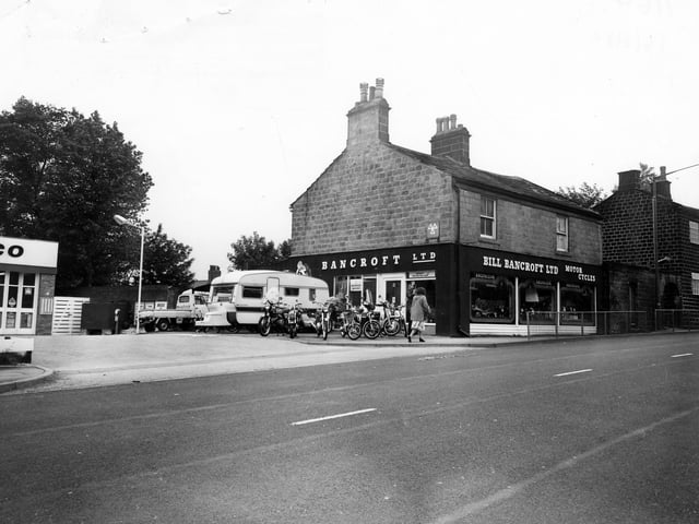 Bill Bancroft Ltd. Motor Cycles on New Road Side in Horsforth. The adjoining property is number 181 New Road Side. Various motor cycles are on diplay in the windows of the showroom and there are more parked outside alongside a caravan. The firm advertises as a Honda Specialist. To the left there is an Amoco Service Station.