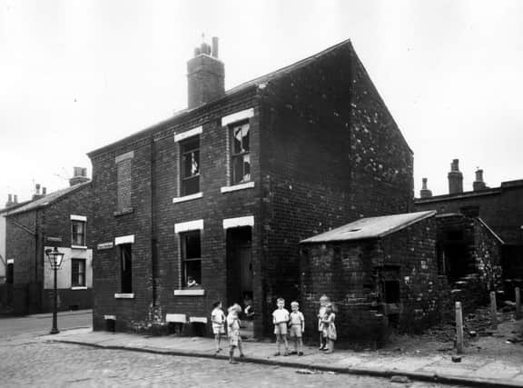 A derelict block of back-to-back houses on Temple View Grove is used by children as a playground. More children stand in the street in front of a derelict outside toilet block. On the left is Temple View Road. Pictured in July 1963.