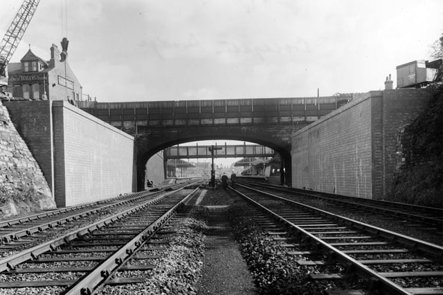 The view looking east along the railway and under Cross Gates Bridge on Station Road. Two men are stood on the railway tracks. To the left of the photograph one can see a small crane. Behind the crane on Station road is the Station Hotel. Pictured in September 1954.