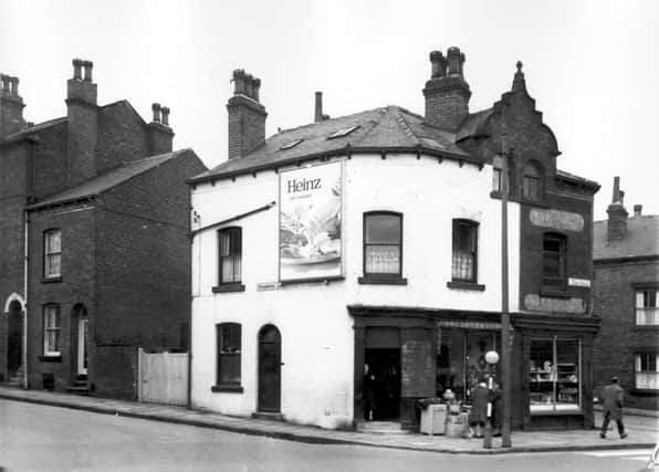 On the left edge of this view from  May 1965 is the single front of number 4 Strawberry Lane. Two shops on Tong Road follow to right, with a Dutch gable style roof above the top two windows. To the left, painted white, is number 170, a second hand furniture shop with a selection of cupboards outside. A blackboard with a chalked price list hangs next to the door. On the side wall is a billboard advertising salad cream with the slogan 'Heinz of course'. Number 168 follows to the right. This is Fred Brown's off-license and tobacconists.