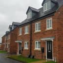 Brand new orange-bricked council homes with neat, grassy gardens in front of them on a cloudy day, with more homes being constructed in the background.