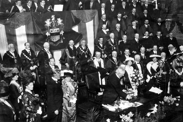 A ceremony is taking place in Morley Town Hall in honour of the Prime Minister, Herbert Henry Asquith 'illustrious son of Morley'. He is receiving the casket containing the scroll of the Freedom from the Mayor, Mr. William Law Ingle entitling the Premier to the freedom of the Borough of Morley. The ceremony was attended by many dignitaries, including the Mayors and Mayoresses of other important West Riding Towns. Mr. Asquith's daughter, Violet stands to the right. She wears a wide brimmed light coloured hat and matching outfit, and carries a large bouquet of flowers. Pictured in July 1913.