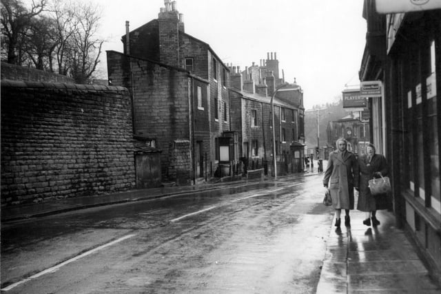 Two women with coats and bags walk along Brunswick Street in 1962. Fieldsend grocers shop on the right has hanging signs advertising Lyons cakes and Ice Cream, also Players cigarettes.