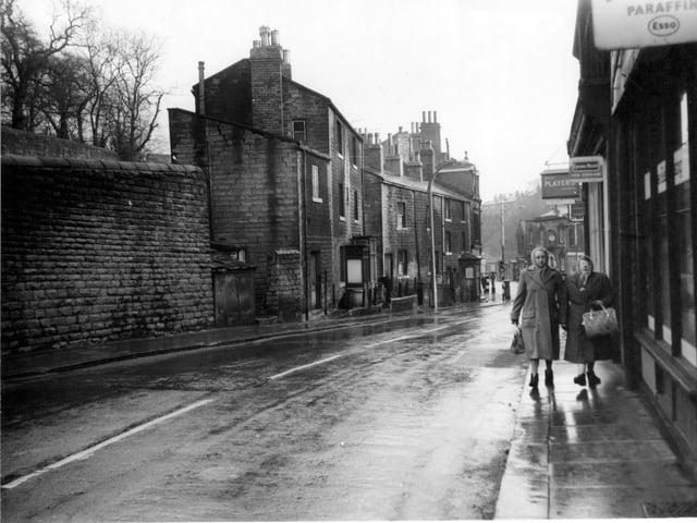 Two women with coats and bags walk along Brunswick Street in 1962. Fieldsend grocers shop on the right has hanging signs advertising Lyons cakes and Ice Cream, also Players cigarettes.