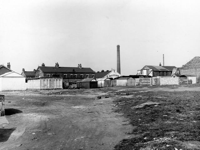 The waste ground on the corner of Compton Road and Florence Street in May 1953. There are several sheds and what looks to be a custom made van in the centre. To the right are two brick buildings, one with an advertising hoarding. The other building has a pile of timber leaning against it. In the distance are three rows of terraced brick houses and to the right of these is the Western cinema.