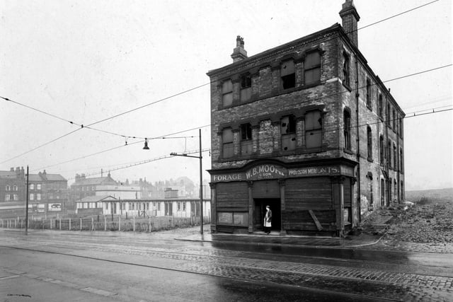 The former premises of W.B. Moore & Son, provision merchants on York Road. The building is derelict, with broken windows and shutters on ground floor windows. A man is standing in the doorway. To the left is a day nursery with some terraced houses behind. Pictured in July 1951.