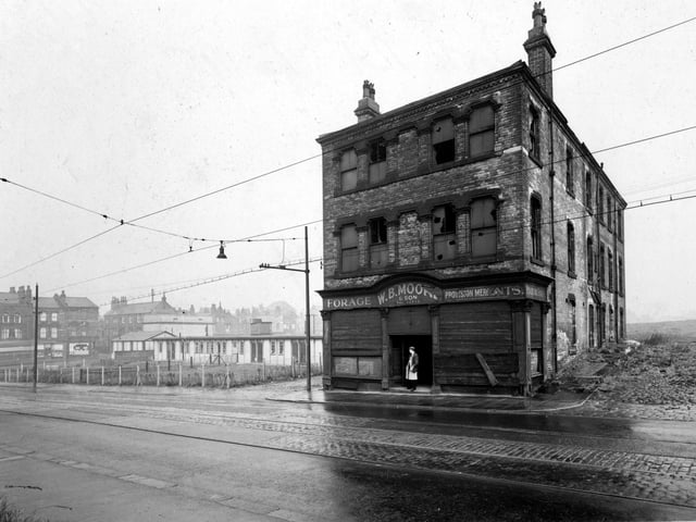 The former premises of W.B. Moore & Son, provision merchants on York Road. The building is derelict, with broken windows and shutters on ground floor windows. A man is standing in the doorway. To the left is a day nursery with some terraced houses behind. Pictured in July 1951.