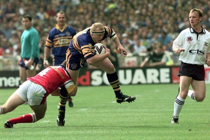 Australian forward Jamie Mathiou takes the ball up for Rhinos, watched by referee Russell Smith.
