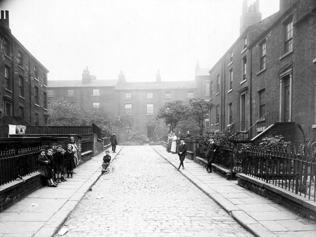 Montrose Street in Leeds city centre pictured in August 1913. In the background is South Carnaby Street. The gardens have low brick walls with railings and some have steps up to the front door. A man, women and children can be seen on the street, which has stone sets.