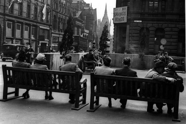 A view looking south from the Museum Rest Gardens along Park Row in September 1943. People are sitting on benches in the concreted area. On the right is Midland Bank Ltd., (at Nos.33 to 35 Bond Street), which has a poster for Savings Bonds on it. Cars and a tram are on Park Row, on the left, with Nos.2 and 3, Marshall & Snelgrove Ltd., department store visible.
