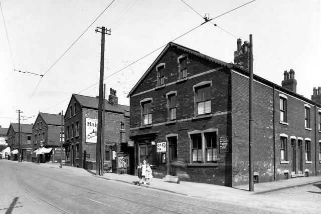 Three girls pose for the camera on Stoney Rock Lane in June 1939. From the left, the first street to intersect with Stoney Rock Lane is Back Fraser Terrace, then moving right, numbers 78/80 shop run by Leonard Smith grocers and off-licence. This shop has blinds down and John Smiths 'Magnet' ales sign. Next street is Fraser Terrace. Number 76A is Frederick Green Hairdresser, a barbers striped pole is projecting from the shop. Number 76 is the home of Michael Rogan a bus cleaner. This junction is with Back Fraser Street. Number 74 is Mrs Clara Fraser sweet shop, the name 'Nixon' is above the shop window.