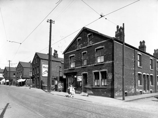 Three girls pose for the camera on Stoney Rock Lane in June 1939. From the left, the first street to intersect with Stoney Rock Lane is Back Fraser Terrace, then moving right, numbers 78/80 shop run by Leonard Smith grocers and off-licence. This shop has blinds down and John Smiths 'Magnet' ales sign. Next street is Fraser Terrace. Number 76A is Frederick Green Hairdresser, a barbers striped pole is projecting from the shop. Number 76 is the home of Michael Rogan a bus cleaner. This junction is with Back Fraser Street. Number 74 is Mrs Clara Fraser sweet shop, the name 'Nixon' is above the shop window.