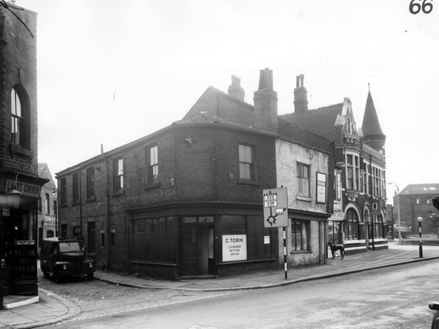 On the left edge of this view, the doorway of Lake's corner, a grocers run by Frederick Lake can be seen on Holbeck Lane. The entrance to Stead Street follows to the right where a van for John Cooke and Son of Huddersfield is parked. This firm were concrete engineers and had works on Coleman Street nearby. Continuing right is C. Tobin's licensed betting office at number 77. Outside this shop is a road sign directing motorists along Wortley Lane to Huddersfield and Halifax and along Spence Lane to Armley.  Pictured in March 1965.