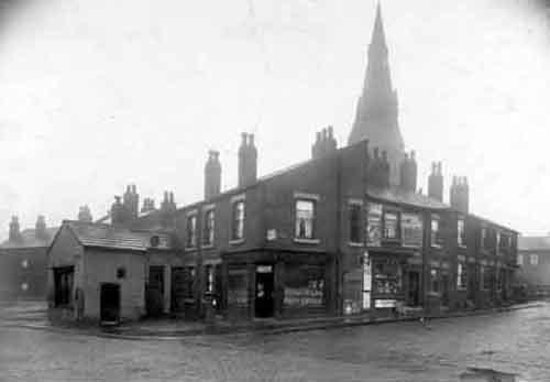 A view from the junction of Wortley Lane with Holbeck Lane in November 1929. It shows the Post Office at the end of Holbeck Lane with the name S.A. Westerman above. Seen to the right is a shop with advertisements outside, including Mansion polish, Lyon's jellies, Hudson's Soap, Brooke Bond Tea, Capstan cigarettes. The Church spire is that of St. John The Baptist.