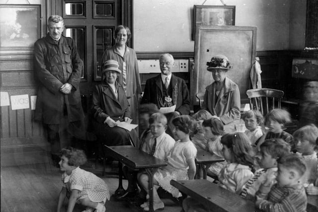 A visit by the Lord Mayor, Alderman Hugh Lupton and the Lady Mayoress, Ella Lupton, to Roundhay Road Council School in  June 1927. The Lord Mayor is wearing his chains of office and the Lady Mayoress is seated to the right of him. The school room is typical of the period with wooden desks containing inkwells arranged in rows. Words and numbers are pinned up around the walls and there is a blackboard at the rear. The children are smartly dressed but there is no uniform.