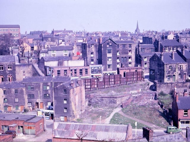 A view overlooking Morley Bottoms taken from Troy Road in April 1962. The image shows how the valley slopes have been built on from Bank Street to Chapel Hill and to Station Road. Demolition has taken place, during the inter-war years, of shops on Chapel Hill (now replaced by rusty advertising hoardings), of housing around the steps from Chapel Hill to Station Road, and in Red Lion Yard in the foreground. Some of the buildings by the paper shop on Station Road disappeared shortly after this picture was taken, as did the Carrier's Arms and houses in Webster's Yard. The Prospect Mills (left) and St. Peter's Parish Church (right) break the horizon.