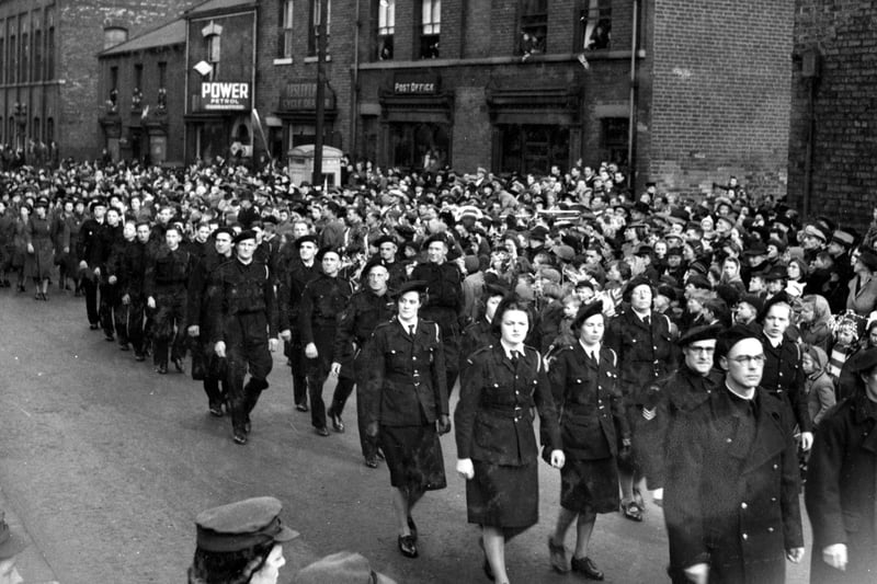 Air raid wardens on parade on Rothwell's Marsh Street during the visit of H.R.H. Princess Mary, The Princess Royal to mark Salute the Soldier Week. The street is lined with men, women and children. Businesses featured are a Post Office and Lesley Pyle, cycle dealer.