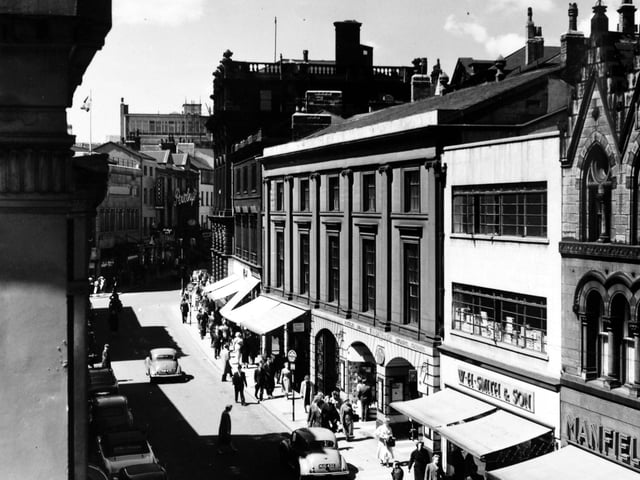A view of Commercial Street from an upper storey window in may 1957. Various shops and businesses are visible, including, at the right edge, Manfield & Sons Ltd., shoe retailers at number 14 Commercial Street. Moving left, the newsagents business of W.H. Smith & Son Ltd occupies number 16 and the ground floor of number 18 (with the arched entrance and windows). Leeds Library has occupied the upper storeys since 1808. The view is towards the junction with Albion Street.