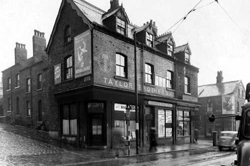 A row of shops on Chapeltown Road in November 1949. On the corner with Cambridge Terrace can be seen Edith Walden, ladies hairdresser. Next door is Sherman's Pools Ltd., with Taylor Bros., tailors, above. On next corner, with Cambridge Place, is C.A. Benjamin, dispensing chemist. A tram fare stage can be seen outside Walden's and a poster for National Savings is on the side of the wall. Cars in street, letter box on corner of Cambridge Place.