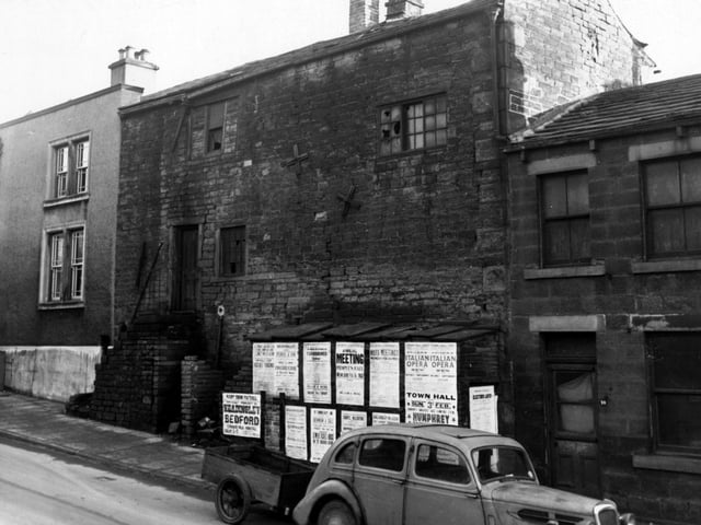 Derelict houses on Pratt's Row pictured in February 1952. A car and trailer are parked outside. Posters for upcoming Leeds events are pasted on the wall.
