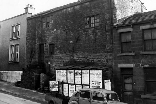Derelict houses on Pratt's Row pictured in February 1952. A car and trailer are parked outside. Posters for upcoming Leeds events are pasted on the wall.