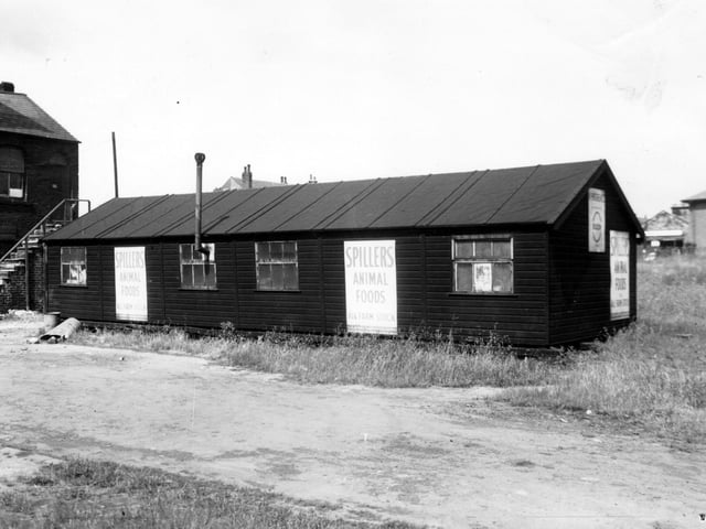 A one-storey wooden construction in Dunderdale Yard in March 1965. Signs for Spiller's Animal Foods are visible. The building also has a venting chimney through one of the windows. On the left edge, the former Crown Chemical Works premises can be seen.