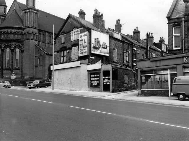Wholesale clothing warehouse on Roundhay Road in April 1980. The front is boarded up and there are advertising hoardings on the upper floor. St. Aidan's Church is on the left with Elford Place leading off. On the right is Back Elford Place.