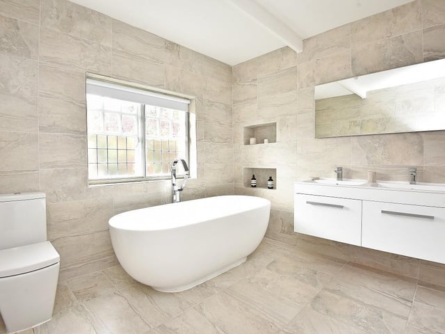 A modern bathroom features twin wash basins with vanity units and a deep free standing bath tub.