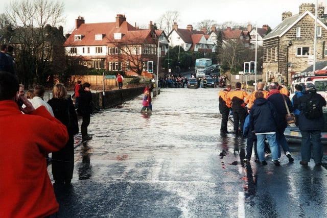 The flooding of the bridge when the River Wharfe broke its banks in April 2002. People wade through the water, cars and lorries queue up unable to cross and men in orange and black wetsuits prepare a rubber dingy.