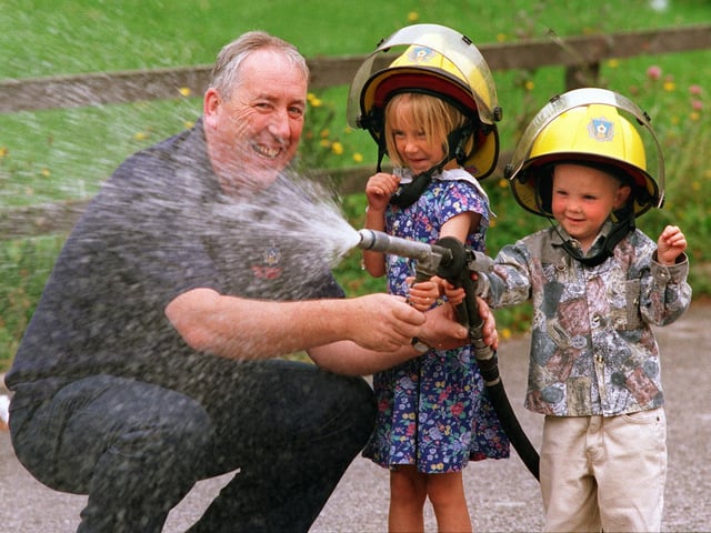 Charlie MacNeill, education officer for West Yorkshire Fire Brigade,  watches as  Zara Carrington and Peter Cummins take over the fire hose  at the Special Kids in Need (SKIN)  playscheme at Halton Moor. Pictured in July 1997.