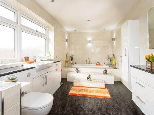 Steps lead up to a sunken bath, and there's a walk in shower cubicle with waterfall shower head in this glossy bathroom.