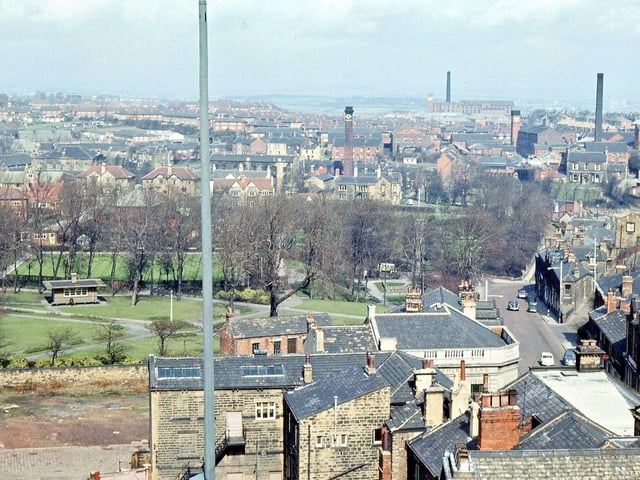 Looking north-west across the town from the bell balcony of Morley Town Hall in April 1965. The nearest object to the camera is the flagpole on the Town Hall roof. The buildings in the foreground are part of Princess Street, not yet cleared, and rooftops of buildings along Queen Street, beyond Lloyd's Bank. There are still plenty of elm trees left in the park, and, of the old housing seen, there is Morley Hall, Prospect House and Yew Tree House. The three mill chimneys seen from left to right belong to Benn and Webster's Victoria Mill, Hield Bros. of Springfield Mills and J. & S. Rhodes of Prospect Mills.