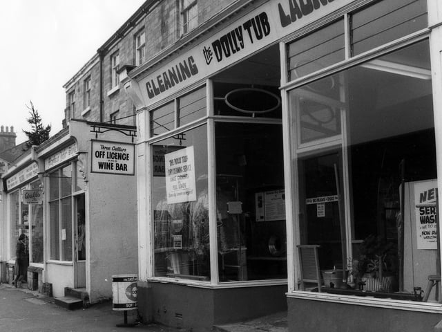 A row of shops on Boston Spa High Street in March 1979. In the foreground is the Dolly Tub Launderette, with the entrance to the Three Cellars off licence and wine bar to the left. Next to this is Mayfair Hair Studio, then a shop selling fancy goods, stationery and ice cream. On the end of the row is the Spice Box restaurant.
