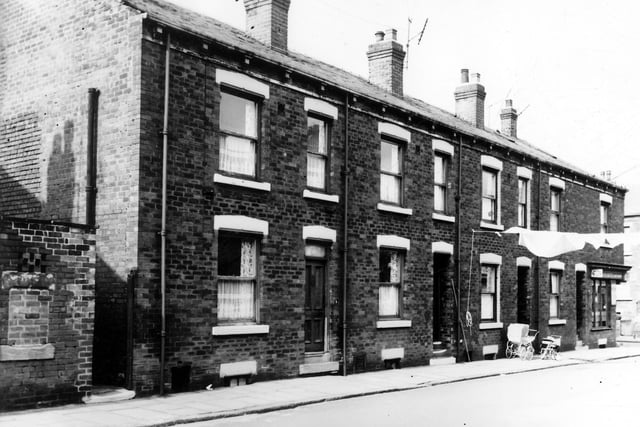 Four back-to-back terraced houses with a yard on the left originally built to house the out on a line stretched across the street from number 6. A coach sprung pram and child's toy pram flank the doorway of number 4. On the far right of the image is number 8 Balmoral Road, steads grocery.