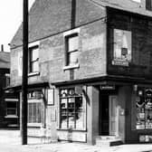 On the far left is Ashton Terrace with number 24 New Pepper Road the E. & V. Allott grocers on the corner. On the right at number 22 is another grocers where an advert for Fry's chocolate can be seen through the door. Products advertised include Tizer, Craven 'A', Wills Woodbines, Lyons Maid ice cream, Senior Service cigarettes and Lyons tea. On the right is Windsor Place where a large poster above the shop promotes Robinsons Lemon Barley.  Two small girls walk along the gable end of the building.