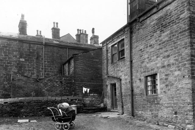 A woman tends a baby in a pram outside number 78, Bell Lane seen from the back garden. Beyond the wall, straight ahead, is a toilet block and in the background, the blind backs of dwellings in Daisy Hill. Pictured in April 1960.