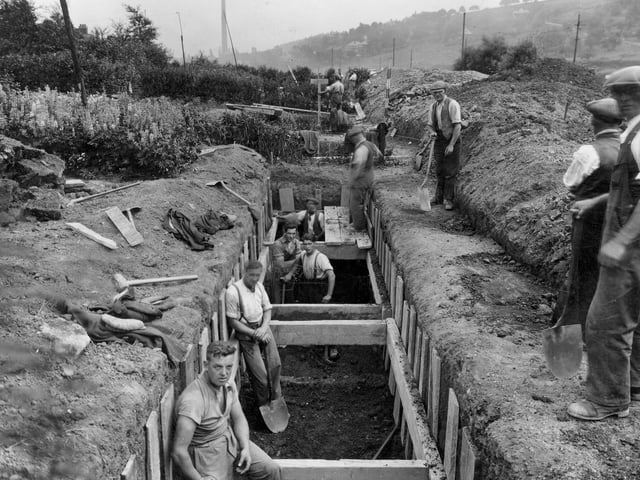 An excavation for a sewer near Meanwood Road. Several workmen are standing in and around a large trench. Woodhouse Ridge can be seen in the background as can a factory chimney. Pictured in July 1937.