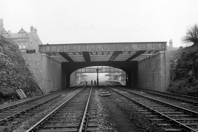 Looking east under Cross Gates bridge towards the station on the Leeds-York railway in February 1955. Workmen, a signal box and the platform are visible. The Station Hotel can be seen in the background on Station Road.