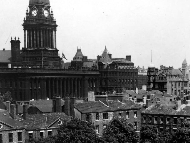 Park Square with Leeds Town Hall in the background pictured in July 1947. Running across the centre are Georgian buildings situated in Park Square North and at the right edge those in Park Square East. The square appears to have unmade paths, sparse grass and mature trees. Nowadays, the buildings are restored and the square is laid out with paths, flower beds and seating.