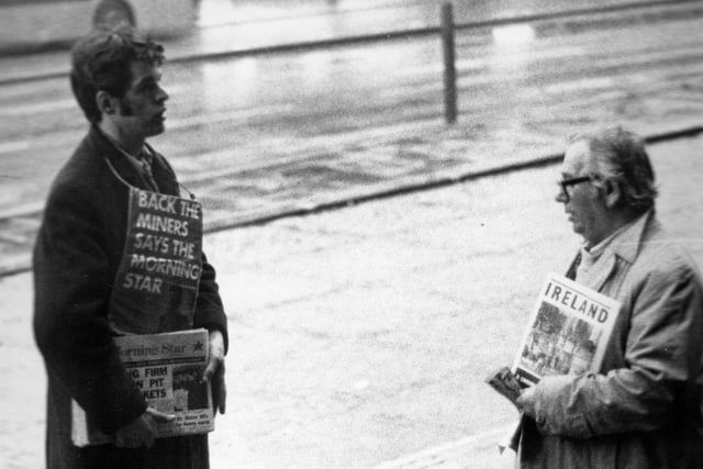 Two newspaper sellers in Leeds city centre engaged in a conversation. The man on the left is selling copies of the Morning Star, a left-wing tabloid newspaper which, until 1966, was known as 'The Daily Worker'. As seen here, the Morning Star was in support of the National Union of Mineworkers during the strikes of the 1970s and 80s. The board strung around the young man's neck states 'Back the Miners Says the Morning Star'. At the time the photograph was taken the miners were part way through a seven week strike for better pay.