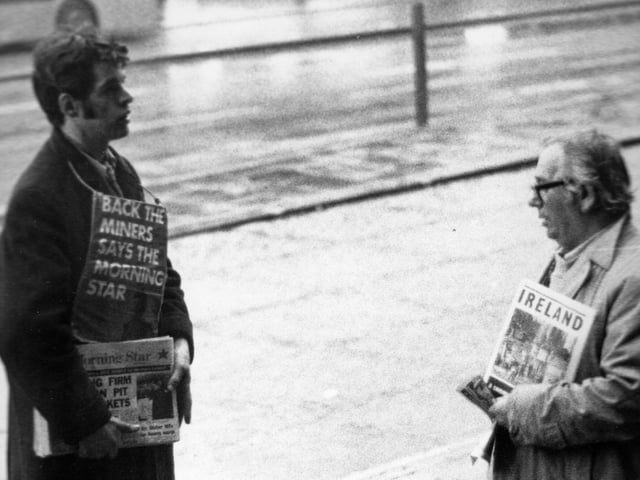 Two newspaper sellers in Leeds city centre engaged in a conversation. The man on the left is selling copies of the Morning Star, a left-wing tabloid newspaper which, until 1966, was known as 'The Daily Worker'. As seen here, the Morning Star was in support of the National Union of Mineworkers during the strikes of the 1970s and 80s. The board strung around the young man's neck states 'Back the Miners Says the Morning Star'. At the time the photograph was taken the miners were part way through a seven week strike for better pay.