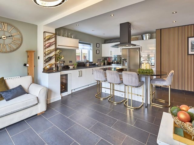 The social family kitchen has white glossy units finished with dark granite worktops which surround an American larder fridge freezer, two wall-mounted ovens and a wine cooler for hosting. There is also underfloor heating.