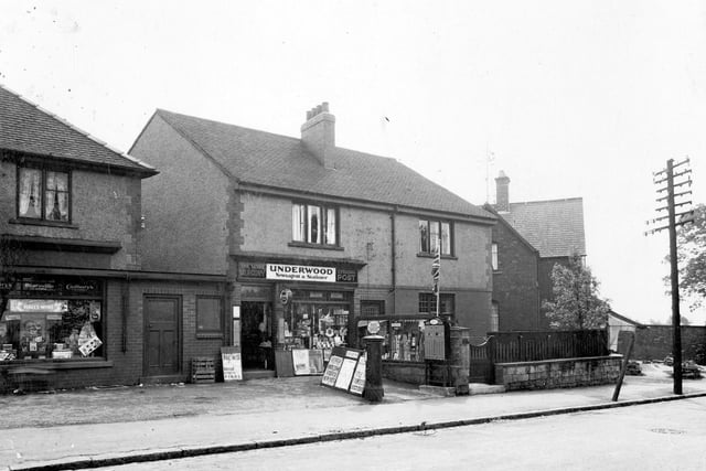 Oakwood Lane in June 1935. On the left is a shop belonging to Thomas R. Blewitt, licensed grocer. The window display has advertising for Halls Wine and Gaymers Cider. To the right, number 393 Philip S. Underwood, Dib Lane Post Office. The Leeds Mercury and Evening Post newspapers are advertised either side of name sign. Street furniture includes a post box, cigarette machine, union jack flag on flag pole, telegraph pole.