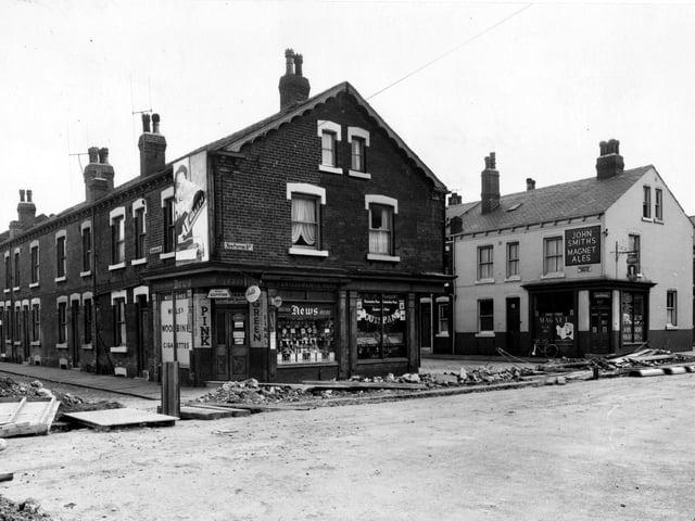 Shops along New Pepper Road in August 1956 showing where a trench has been excavated for sewerage. To the right can be seen end of Rocheford Terrace, with off licence at end. Advert for John Smith's Magnet Ales on wall. Greengrocers and newsagent on opposite corner.